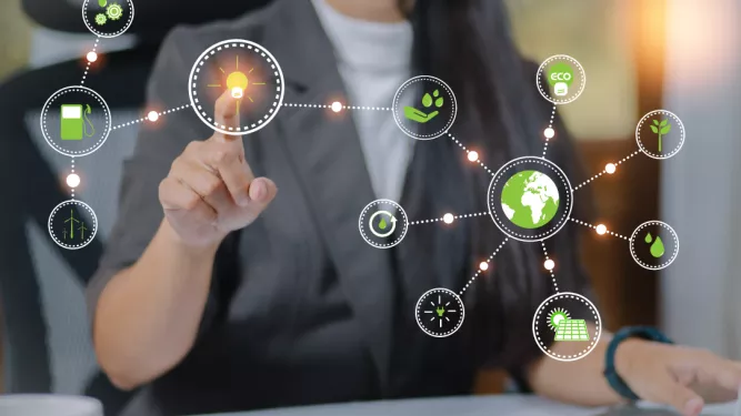 Uma empresária de terno formal toca um ícone iluminado em uma interface virtual que representa a sustentabilidade ambiental. Vários ícones verdes conectados a cercam, incluindo símbolos ecológicos e um globo. Ela está trabalhando em uma mesa com um computador.