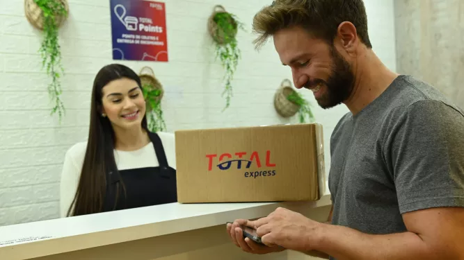 Um casal em pé no balcão com uma caixa escrito "Total Express"