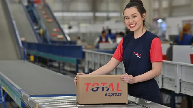 Funcionária de cross docking segurando caixa da Total Express em uma esteira 