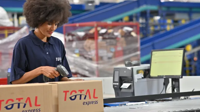 Mulher trabalha no setor logístico empacotando encomendas para distribuição em ponto de coleta