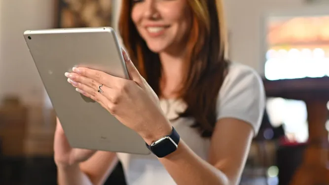 Jovem sorrindo enquanto navega em um tablet e usa um smartwatch, mostrando a facilidade e os benefícios de fazer compras online através do instagram shopping.