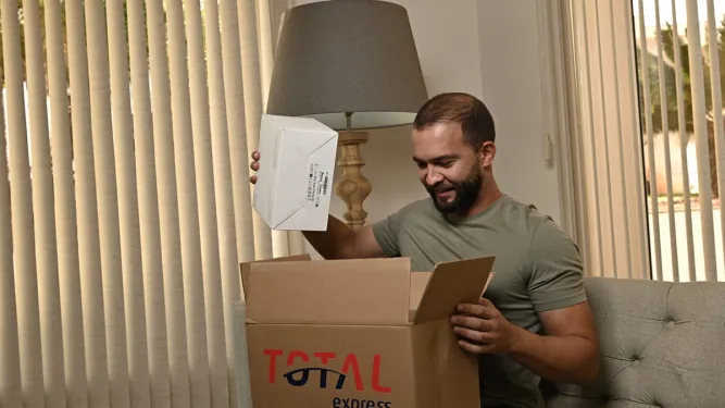Homem sorri ao tirar produto de caixa da Total Express após uma ótima experiência de entrega.