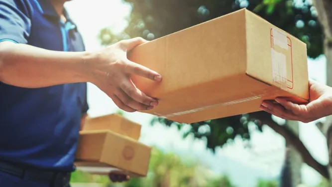 Entregador passa caixa para cliente ao ar livre na entrega de produtos em áreas remotas.