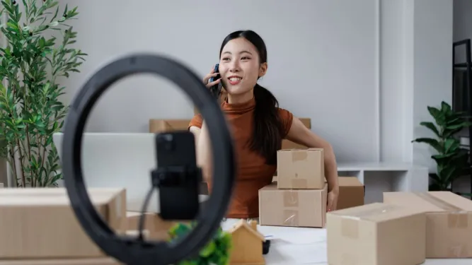 Empreendedora grava vídeo em ring light com caixas, buscando gerar engajamento no Instagram.