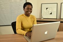 Mulher sorrindo enquanto está sentada em uma mesa com um laptop.