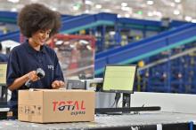 Representação da logística 4.0 com uma operadora fazendo a leitura de uma etiqueta em caixa da Total Express.