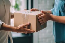 Entregador entrega encomenda nas mãos do cliente. Ele faz parte de uma rede de logística de distribuição