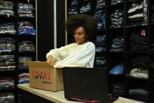 Mulher prepara pacote de envio em uma loja de roupas ao lado de um notebook, exemplificando a operação logística de um DC-e.