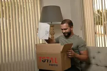 Homem sorri ao tirar produto de caixa da Total Express após uma ótima experiência de entrega.