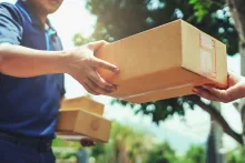 Entregador passa caixa para cliente ao ar livre na entrega de produtos em áreas remotas.