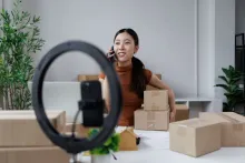 Empreendedora grava vídeo em ring light com caixas, buscando gerar engajamento no Instagram.
