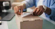 Pessoa colando etiqueta em caixa para serviço de entrega para e-commerce.