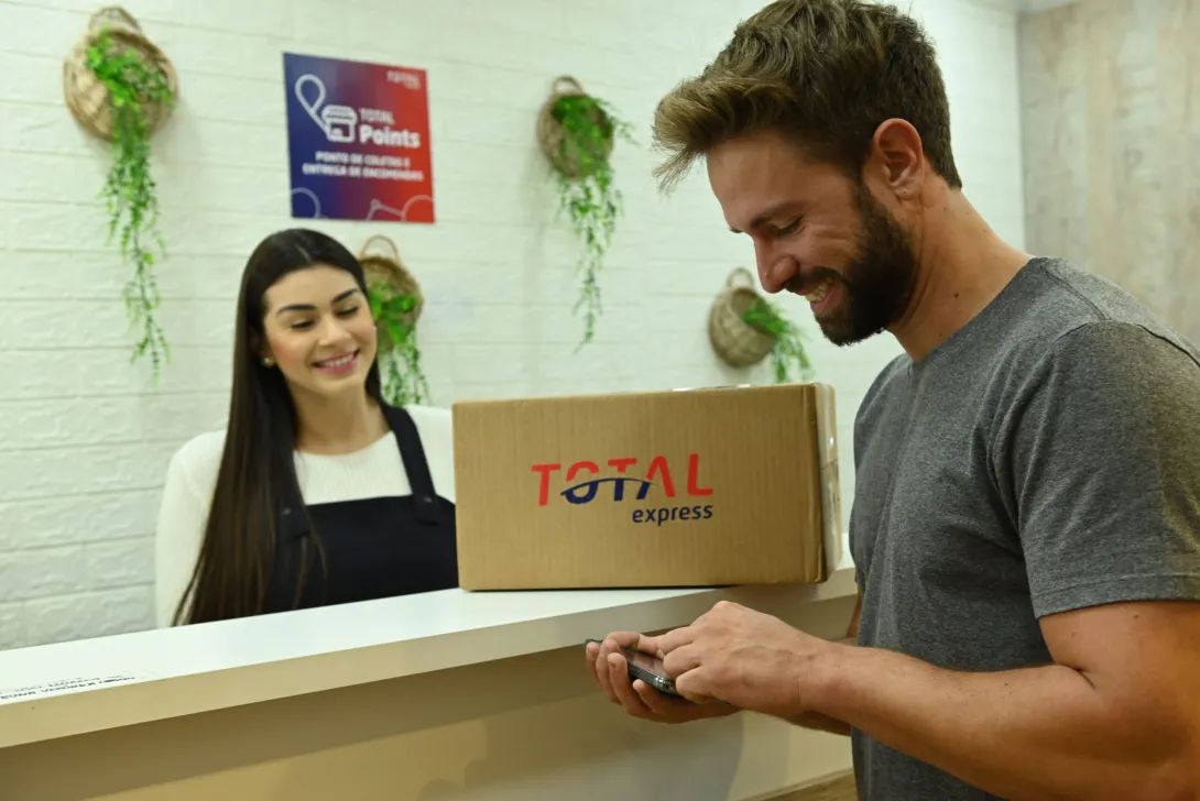 Um casal em pé no balcão com uma caixa escrito "Total Express"