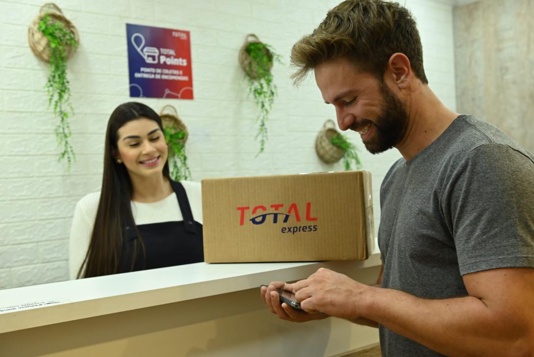 Um casal em pé no balcão com uma caixa escrito "Total Express"