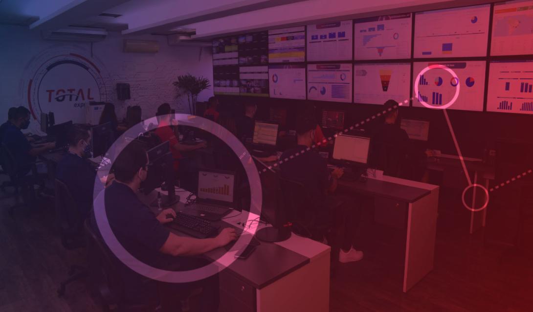 8 pessoas sentadas de frente para computadores trabalhado, as telas representam o sistema de segurança da Total Express, chamado GRIS