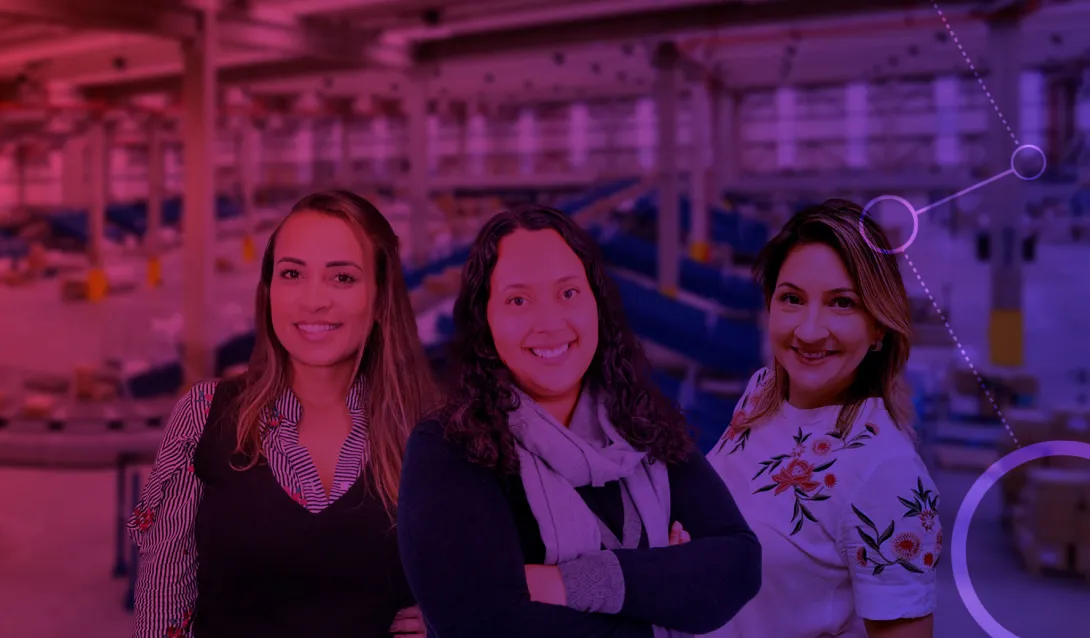 Três mulheres estão lado a lado em frente a um armazém moderno e amplo com uma cobertura roxa. Eles estão todos sorrindo e vestidos com roupas casuais. O fundo apresenta equipamentos industriais e correias transportadoras, com elementos gráficos digitais adicionados.