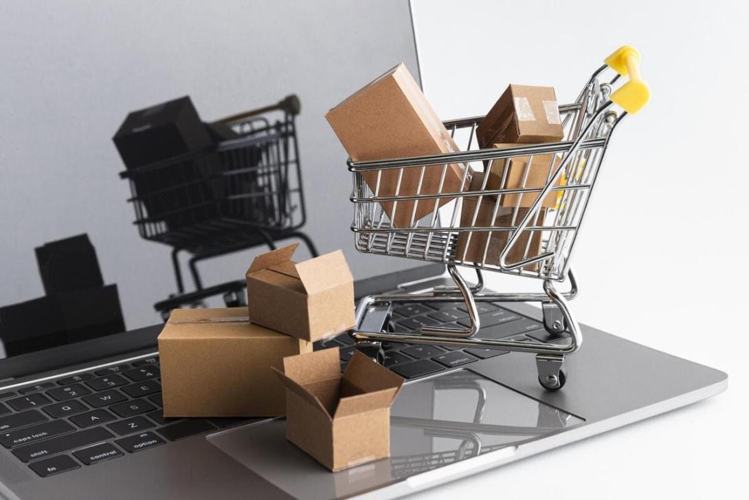 Um notebook aberto e uma miniatura de carrinho de compras em cima com caixas de papelão dentro, representando a Cyber Monday.