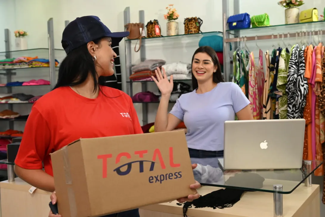 Funcionária de loja recebe pacote da transportadora, representando a etapa inicial da logística de entrega, conhecida como first mile.