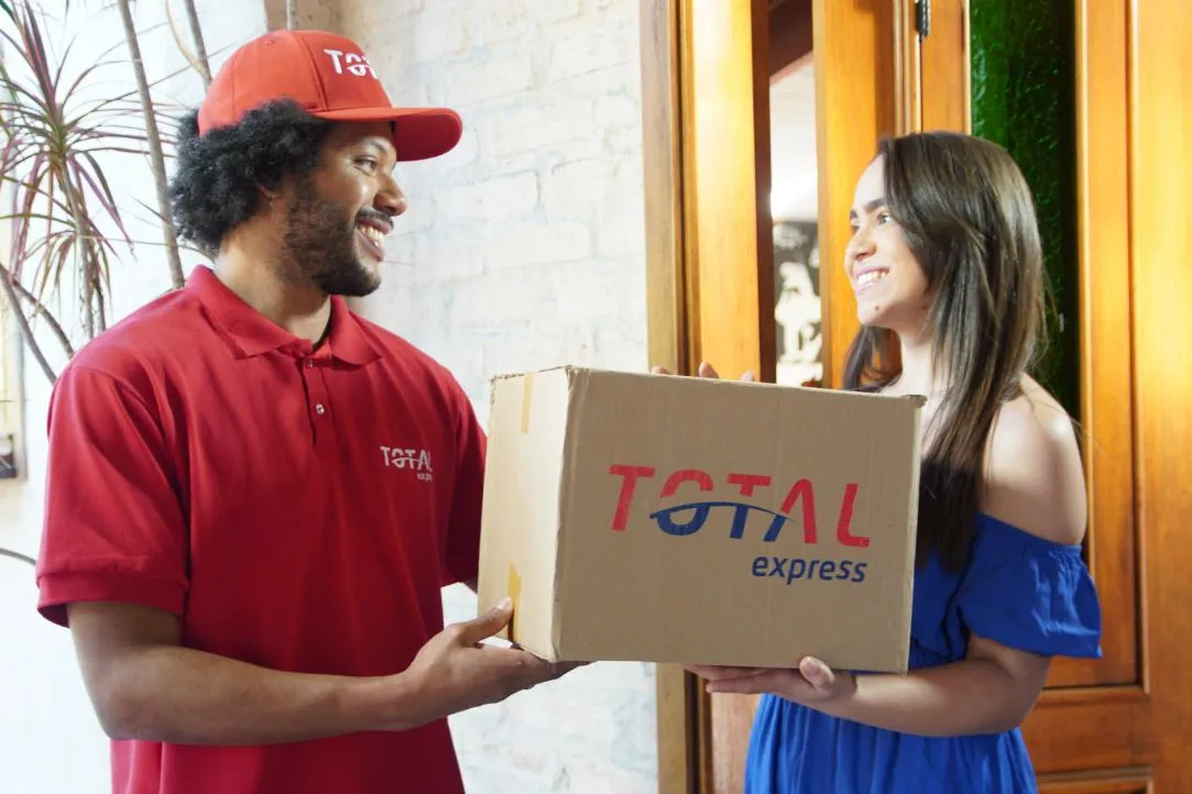 Entregador da Total Express sorri para a cliente enquanto faz a coleta de uma Total Reversa.