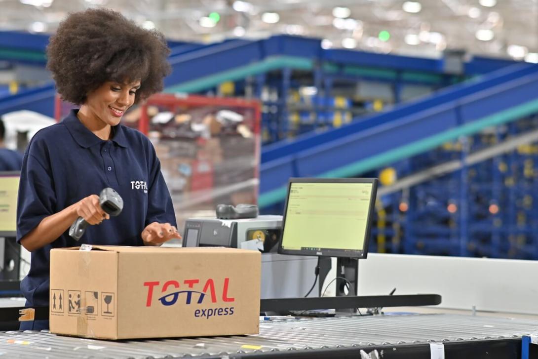 Representação da logística 4.0 com uma operadora fazendo a leitura de uma etiqueta em caixa da Total Express.