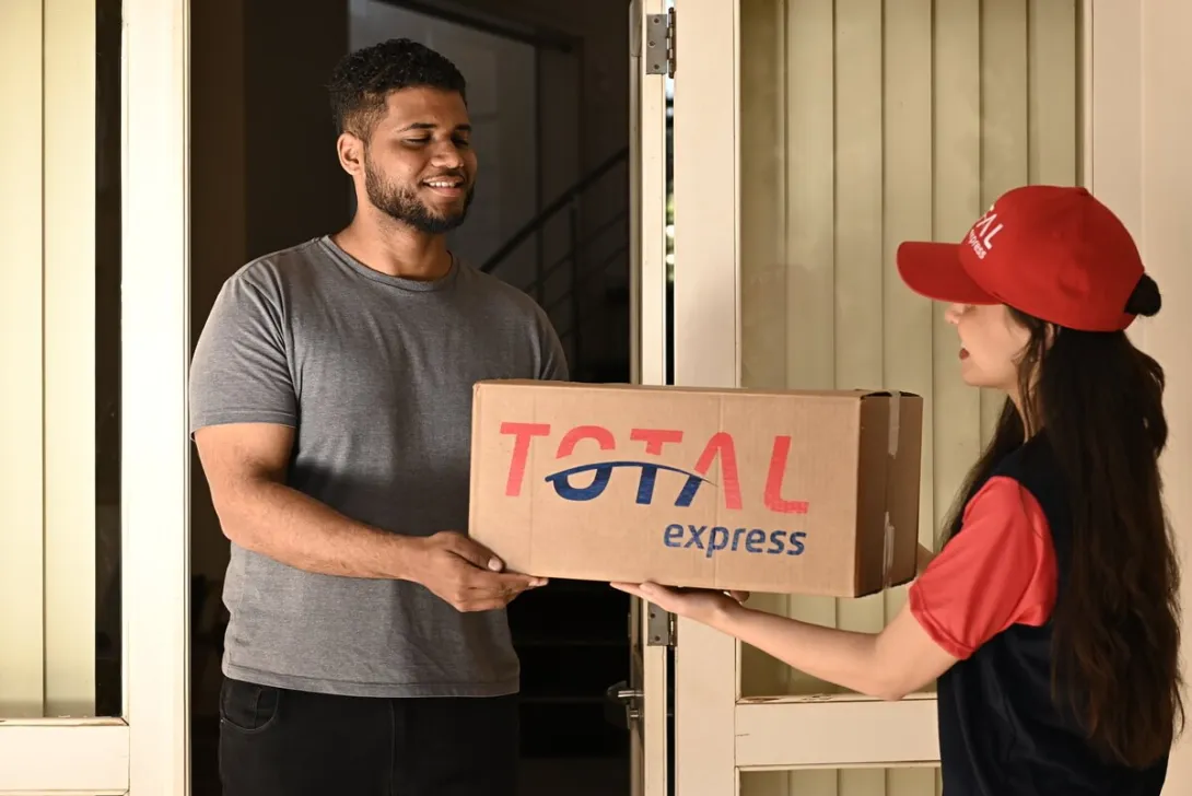 Funcionária da Total Express fazendo uma entrega à domicílio de frete courier a um cliente