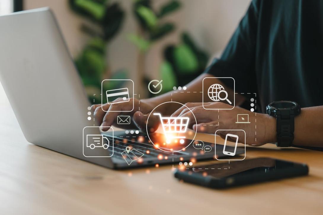 Mãos digitando no teclado de um laptop com ícones de carrinho de compras e e-commerce flutuando, representando o mercado digital.